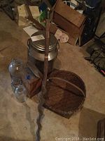 Overview shot showing milk jug, glass jars, walking stick, anvil and basket on concrete floor