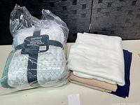 Sealed Berkshire throw with ribbon next to three folded fleece blankets