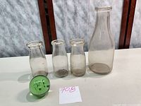 Group shot of four clear glass milk bottles and one green glass paperweight