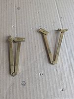 two brass plated folding lid stay hinges on cardboard