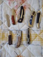 Group image of all eight folding pocket knives laid out on quilt background