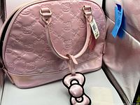 Front view of light pink embossed Hello Kitty handbag with bow charm and tags