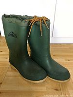 Green Arctic Shield rubber rain boots side view showing logo, drawstring cuff, tan sole