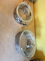 Two assembled casserole dishes showing glass lids and tarnished metal holders