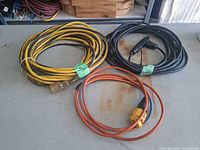 Three coiled extension cords in yellow, black and orange on workbench
