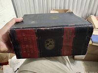 Spine view showing black cover, red panels, gilt emblem, edge wear