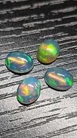 Four oval opal cabochons on dark background showing play-of-colour