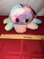 Top view of reversible octopus plush showing pastel colors and happy face next to ruler
