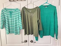 Three green sweaters hanging on doors