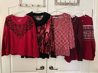Five red-tone sweaters hanging on door