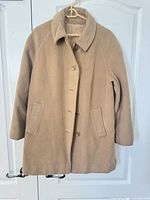 Full view of tan cashmere coat hanging, showing exterior design, buttons, collar and pockets