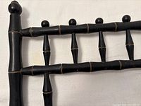Close-up of black painted faux bamboo spindle back rail showing wear and gold accent lines