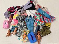All items in lot displayed including clothing pieces, five baby dolls, pink backpack, blue carrier, blankets