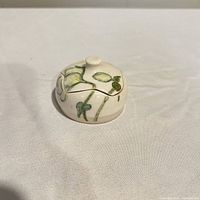 Closed trinket box showing cream glaze and green leaf decoration