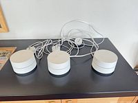 Three Google Wifi routers and power adapters on countertop