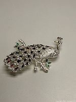 Full view of silver-tone peacock brooch with rhinestones and enamel accents