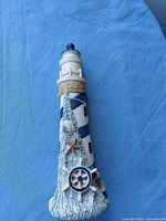 Front view of white and blue polyresin lighthouse with nautical embellishments