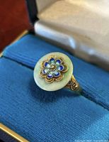 Ring in presentation box showing jade disc and enamel flower