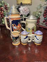 All five steins front view showing designs and lids