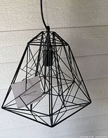 Front view of black geometric pendant light showing wire frame and hanging cord