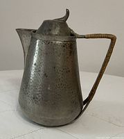 Side view showing conical shape, hammered texture, bamboo-wrapped handle, spout, and lid finial