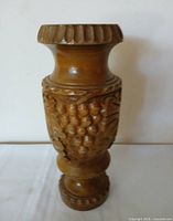 Full view of carved wooden vase front showing grape/leaf relief and pedestal base
