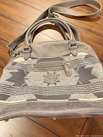 Front view showing woven panel, Roots logo patch, zip pocket, handles and strap