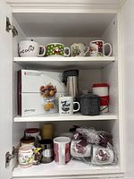 Cabinet shelves containing various mugs, travel mugs, teapot and boxed bowls