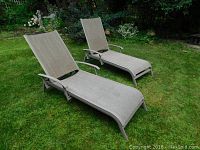 Pair of two garden lounge chairs with metal frames and beige woven fabric, placed on grass outdoors
