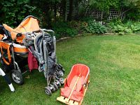 Orange all-terrain stroller, folded grey umbrella stroller, and wooden sled on lawn