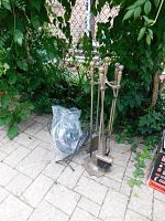 Five-piece fireplace tool set with poker, tongs, broom, shovel, stand with metal log holder and a light fixture shown wrapped in plastic.