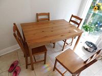 Full view of wood kitchen table surrounded by four wooden chairs on tiled floor near window with natural light.