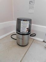 Front view of Cuisinart spice and nut grinder standing upright on the floor with power cord visible.