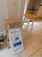 Photo showing the wood step stool, round stool, and packaged plastic shelf all together on tiled floor.