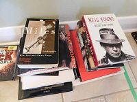 Stack of multiple music books including Miles Davis autobiography, Neil Young Waging Heavy Peace, and Rolling Stones book.