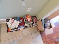 Books stacked on floor and inside open box near wall