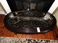 Top view of oval coffee table showing bevelled glass top with bronze-tone metal scrollwork beneath and dark wood frame.