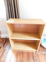Front view of the faux wood two-shelf bookcase showing the two internal shelves and the light oak finish.