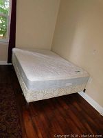 Full view of mattress and box spring assembled on metal frame against wall