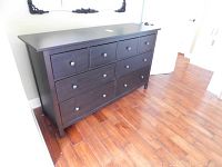 Front view of black wooden dresser with nine drawers, showing slight wear and metal knobs.