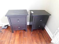 Pair of black end tables viewed from front showing the two drawers and square tops with wear marks.