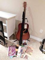 Guitar standing against wall with strap and music books laid out