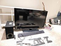 Samsung flat-screen TV with Sony soundbar, active subwoofer, TV wall mount bracket and remote laid out on floor