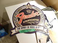 Metal Fender Stratocaster sign showing front view with vintage design, some wear visible.