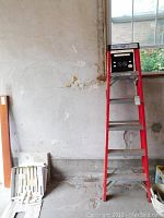 Full view of the red 6 foot metal step ladder upright against a wall with a window in the background.