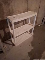 Full view of white 3-tier plastic shelf against concrete wall
