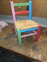 Front angle of the multicoloured wooden child chair showing colours and woven seat