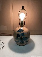 Front view of beige ceramic lamp with blue floral design, bulb, harp and finial visible