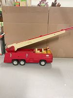 Full left side view showing red metal fire truck with extended cream ladder and six wheels