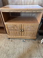 Front view showing open shelf, carved double doors, brass-tone handles, casters
